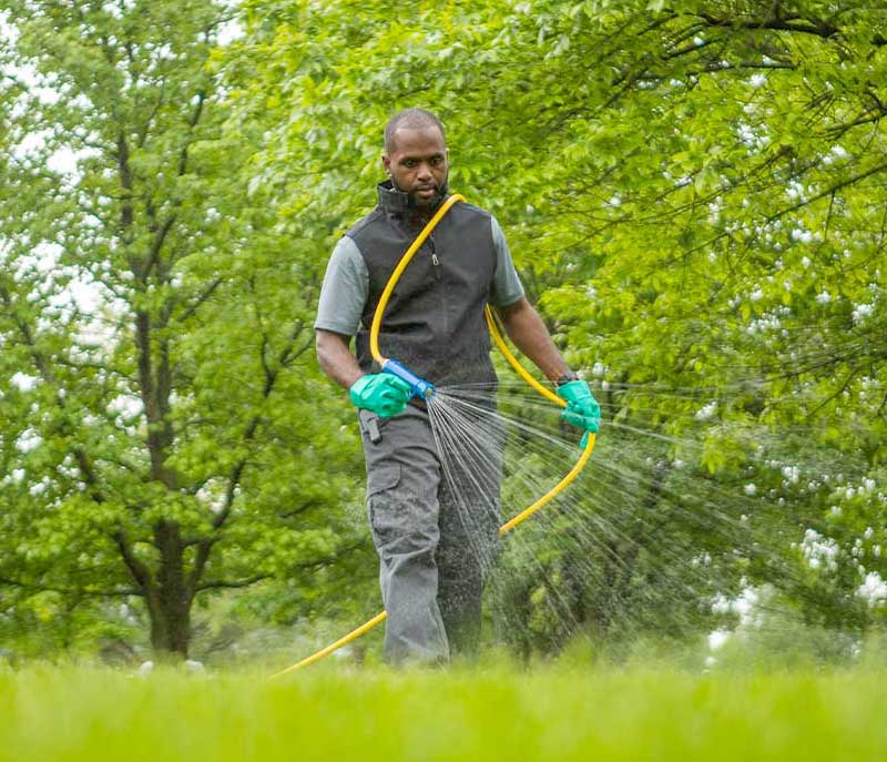 A man standing on a green lawn while performing liquid aeration